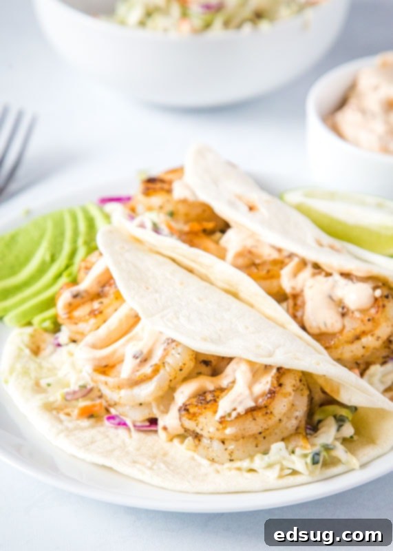 Close-up of fully assembled shrimp tacos in flour tortillas on a white plate