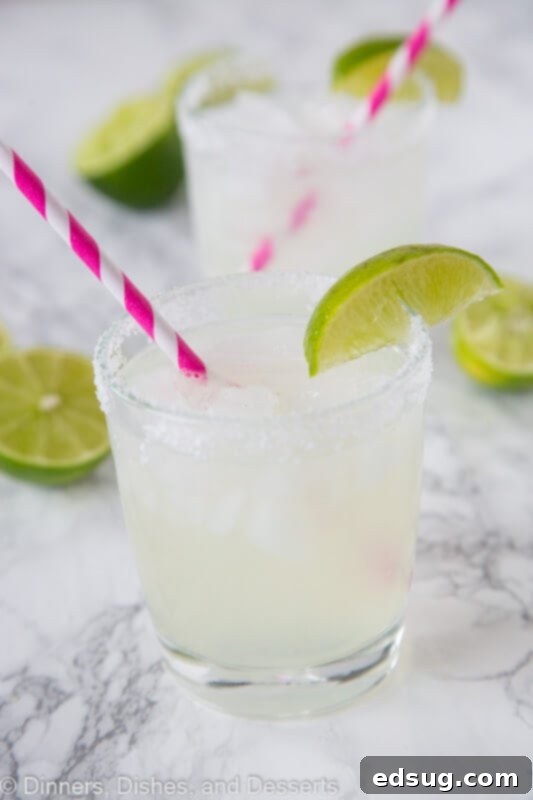 The Quintessential Lime Margarita, On the Rocks 2 Classic lime margarita in a glass with a fresh lime wedge and a pink straw, ready to be enjoyed.