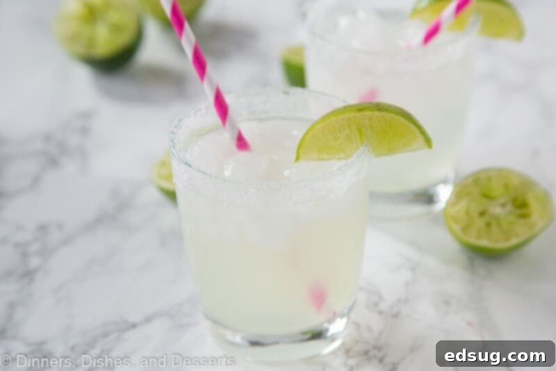 The Quintessential Lime Margarita, On the Rocks 4 Two glasses of classic lime margaritas, with lime wedges and pink straws, sit on a table, evoking a sense of relaxation.