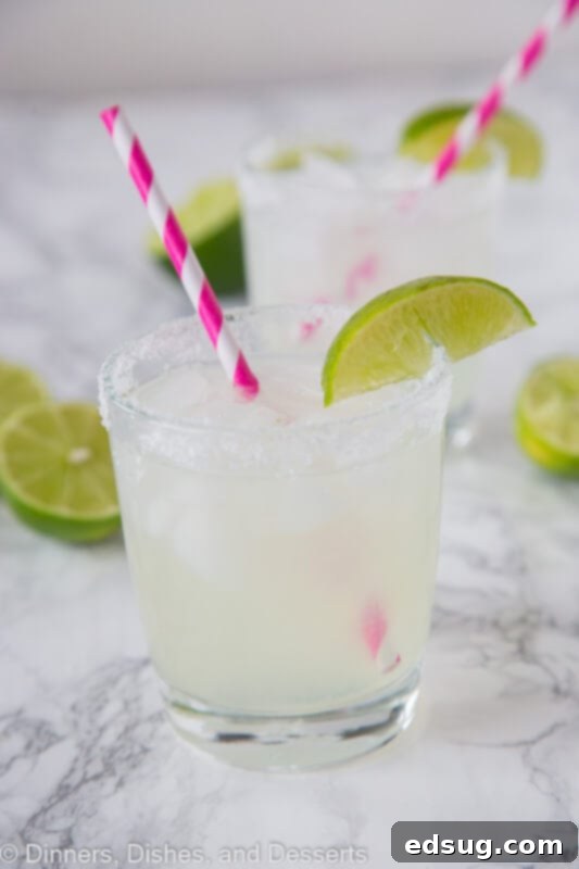 The Quintessential Lime Margarita, On the Rocks 5 A close-up shot of a refreshing classic lime margarita, featuring a vibrant green lime wedge and a cheerful pink straw.