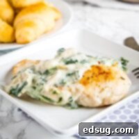 close up white plate with chicken topped with spinach and artichoke sauce