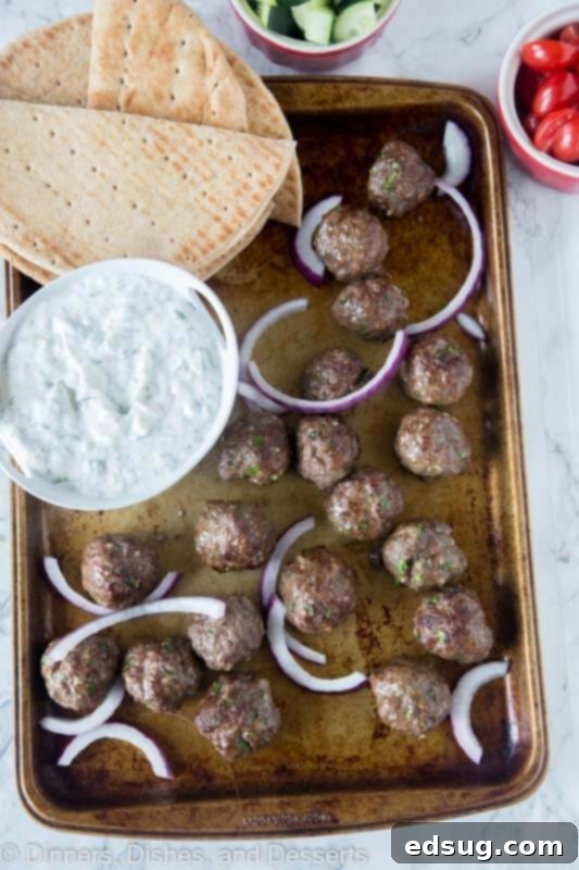 One-Pan Greek Meatballs 2 Sheet pan loaded with freshly cooked Greek meatballs, garnished with vibrant fresh parsley and a bowl of creamy tzatziki sauce for dipping.