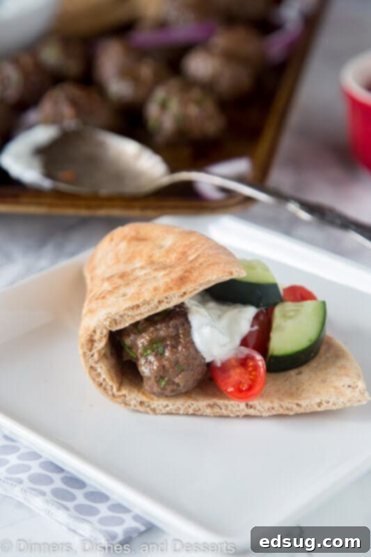 One-Pan Greek Meatballs 3 A perfectly assembled mini gyro with a Greek meatball, tzatziki sauce, and fresh cucumber slices on a soft pita, served on a white plate.
