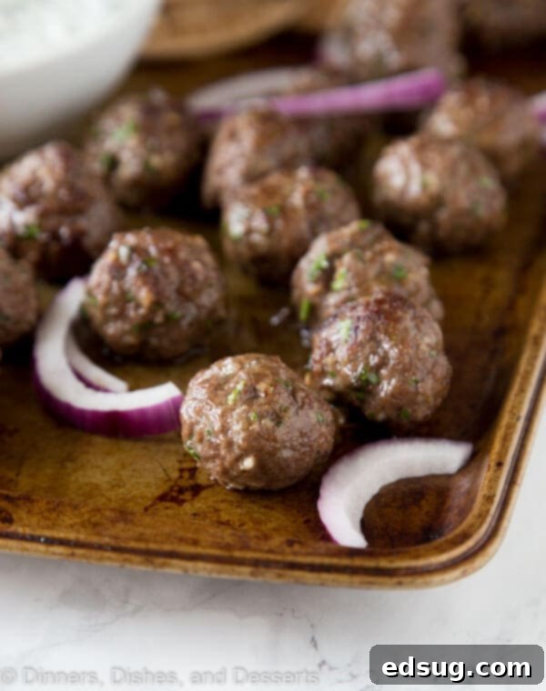 One-Pan Greek Meatballs 4 A sheet pan filled with golden-brown Greek meatballs and sliced red onions, fresh from the broiler, ready to be served.