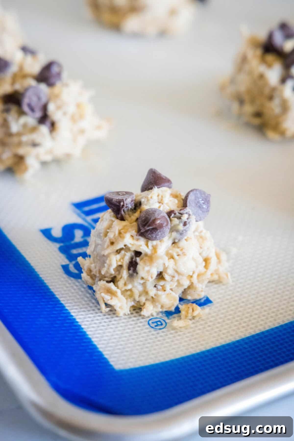 Scoops of banana chocolate chip cookie dough arranged on a parchment-lined baking sheet before baking