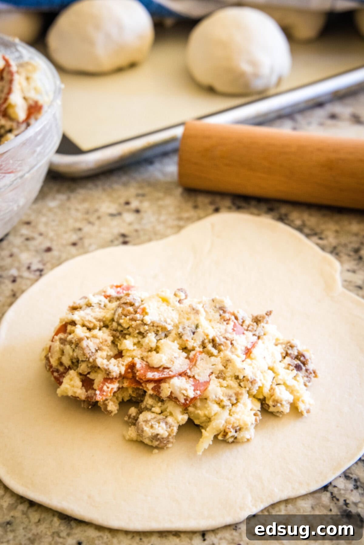 Folded Pizza Pockets 7 Calzone filling spread on one half of a rolled-out dough circle, with an empty border for sealing.
