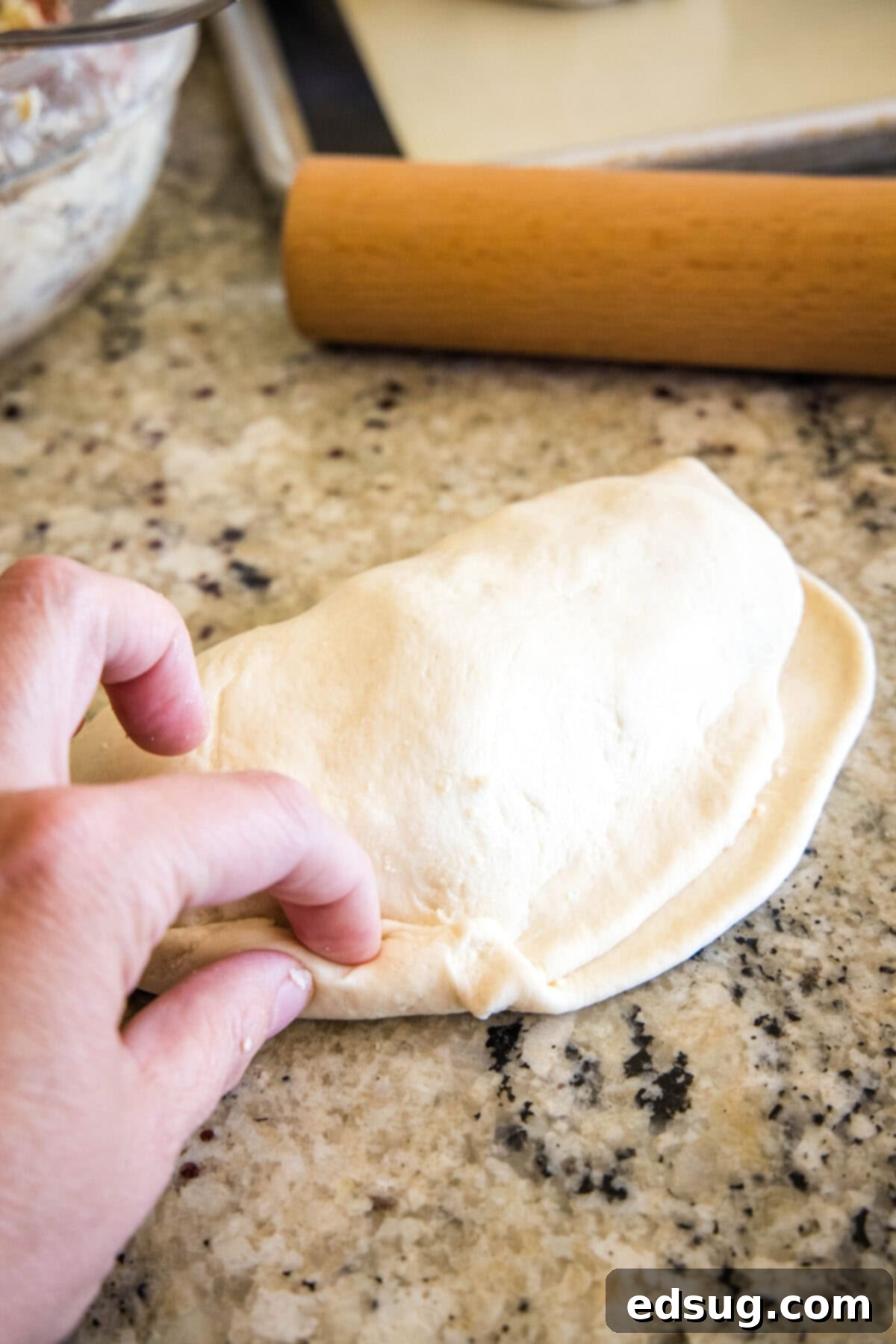Folded Pizza Pockets 8 Hands carefully folding and crimping the edges of a calzone to seal the filling inside.