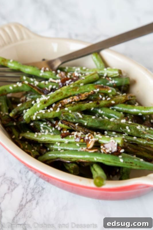 Close-up shot of roasted green beans with sesame seeds in a serving bowl, highlighting the slight char and glistening seasoning.