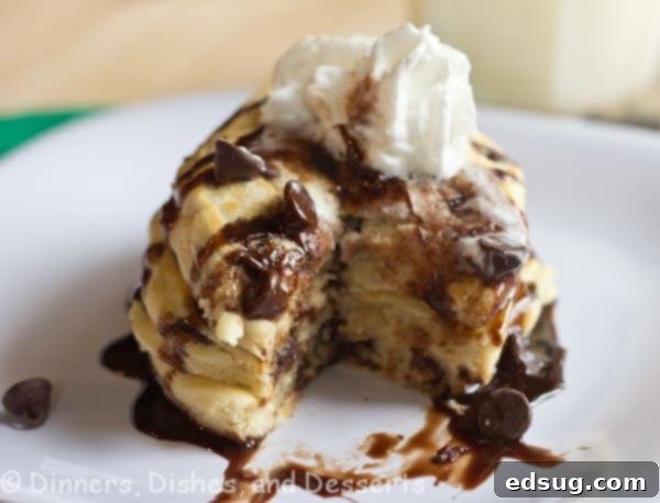 Close-up of fluffy chocolate chip cookie pancakes, golden brown with melted chocolate chips visible, stacked on a white plate. Ideal for a delicious and easy breakfast.