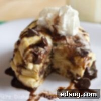 A stack of golden brown chocolate chip cookie pancakes, garnished with whipped cream and chocolate sauce, on a white plate. A perfect sweet breakfast treat.