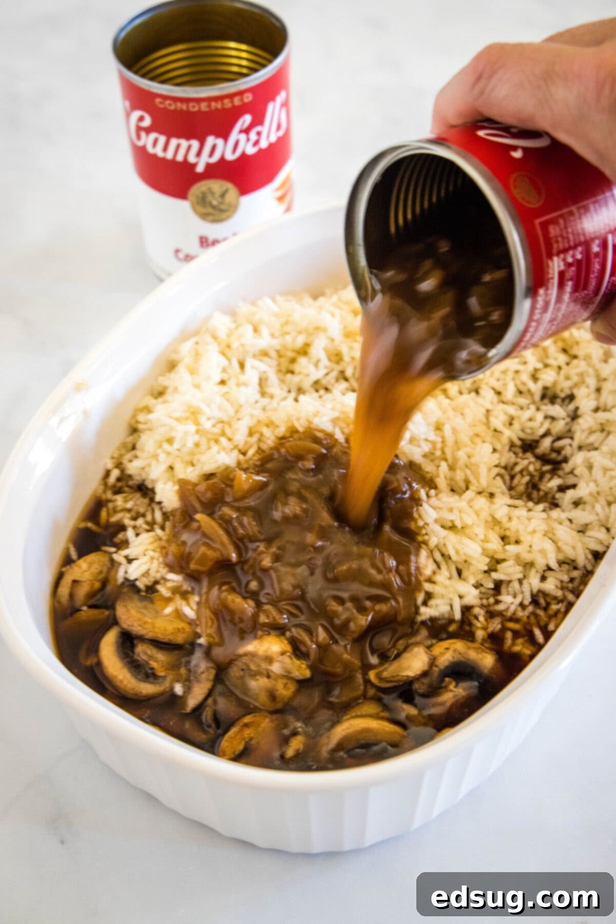 pouring french onion soup into baking dish with rice