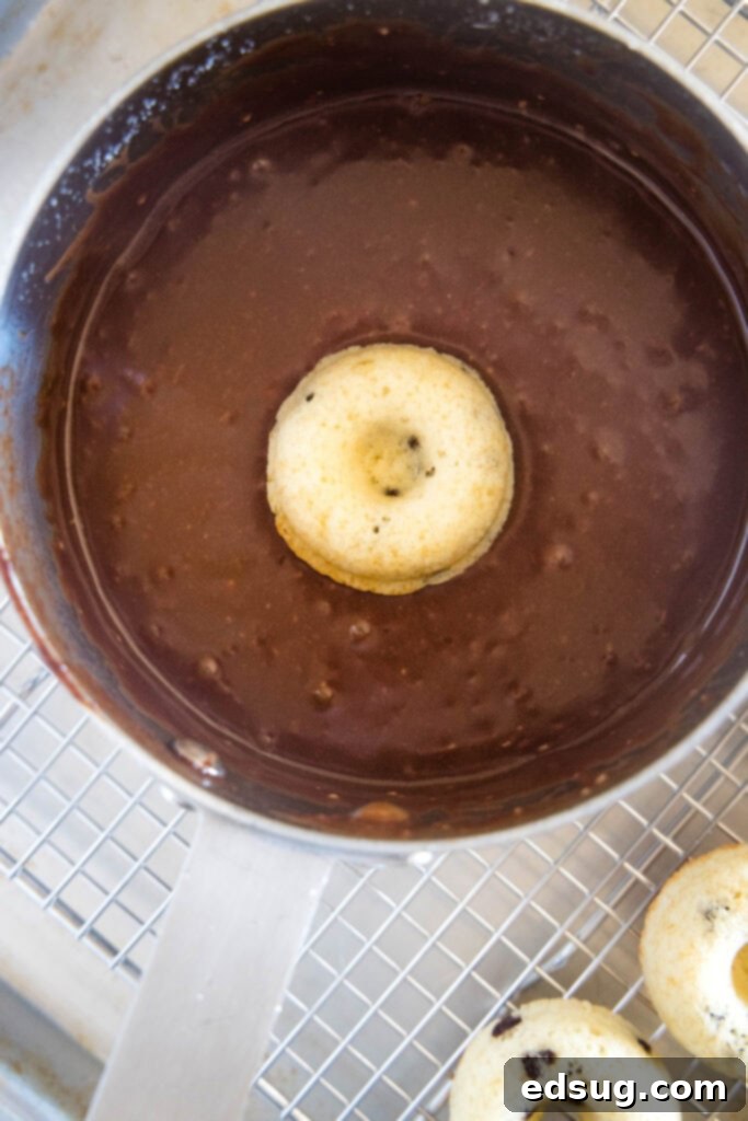 A mini chocolate donut being dipped into a bowl of rich chocolate glaze
