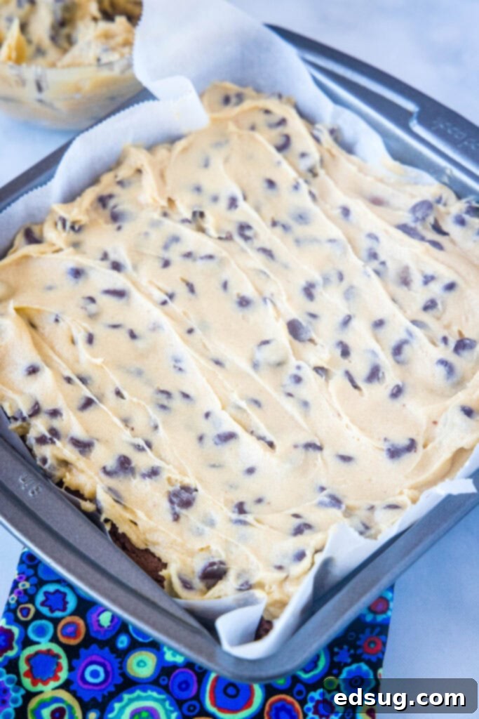 A close-up of fudgy brownies generously frosted with edible cookie dough frosting, highlighting the perfect spread and visible chocolate chips, ready to be enjoyed.