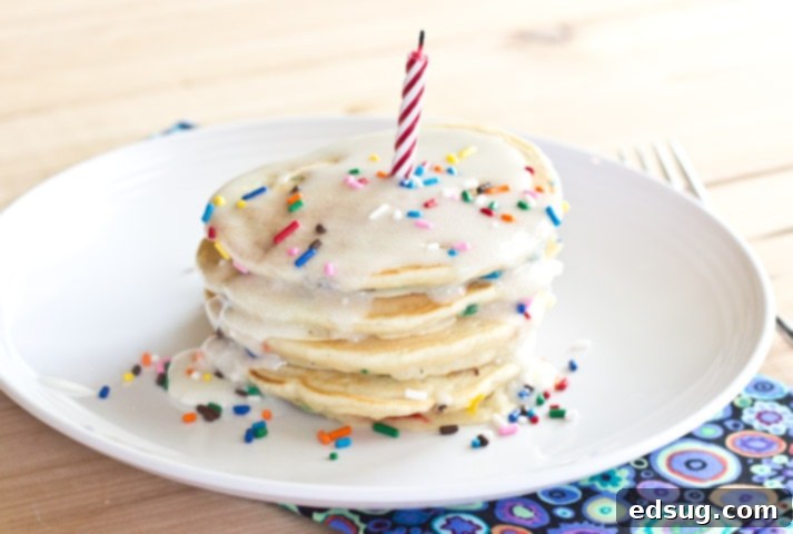 A stack of funfetti pancakes on a plate with a lit birthday candle