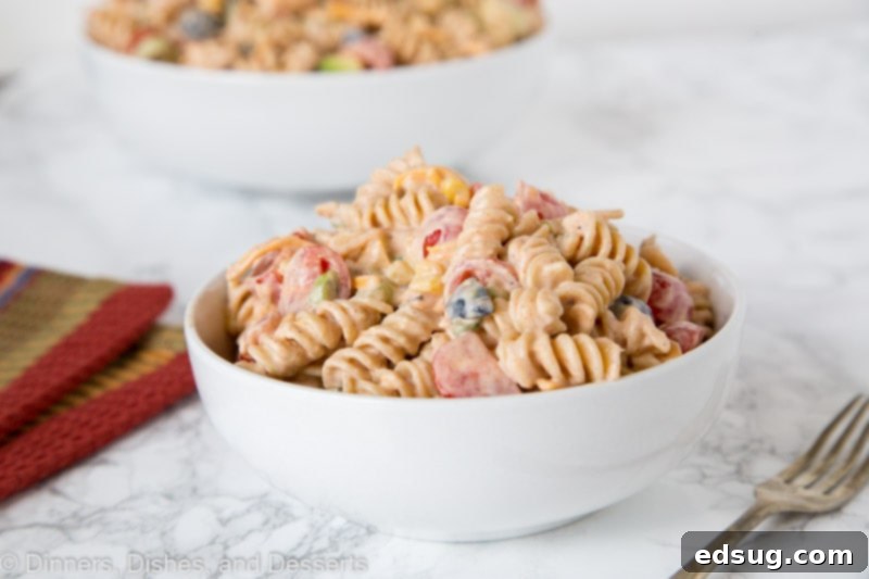 A large bowl of creamy taco pasta salad served on a wooden table, with fresh ingredients visible.