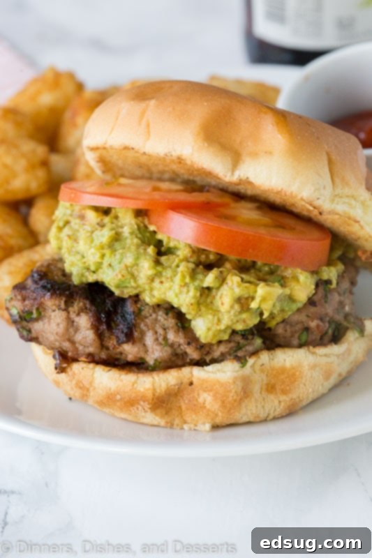 A close up of a turkey burger topped with guacamole and tomato on a plate, ready to be eaten.
