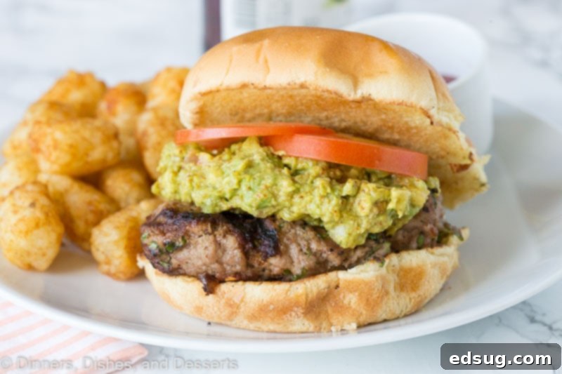 A perfectly grilled turkey burger topped with fresh guacamole and a slice of tomato, served on a bun.