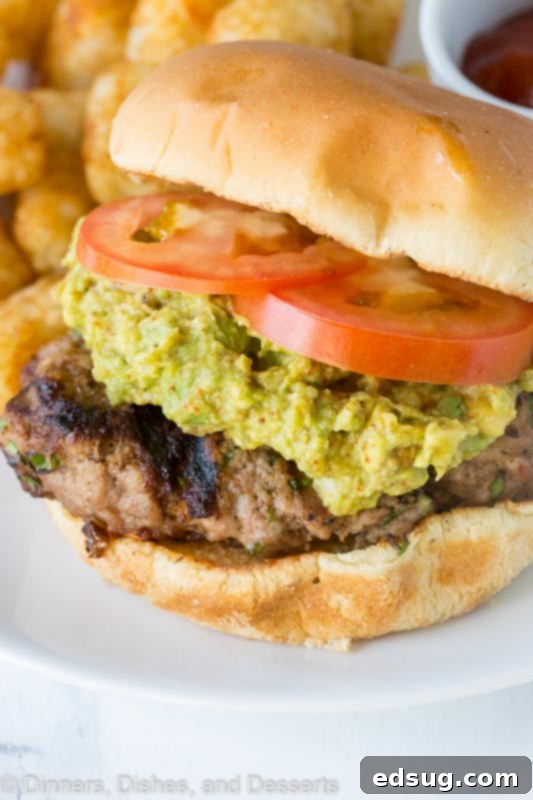 A close up of a delicious chili lime turkey burger, generously topped with creamy guacamole and fresh tomato slices.