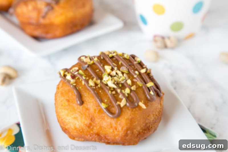Two Nutella donuts on a plate, generously topped with chopped pistachios, ready for serving.