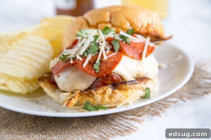 Pepperoni Pizzaburger 4 A perfectly grilled pepperoni pizza burger topped with melted cheese and pepperoni, served on a bun with potato chips on a white plate.