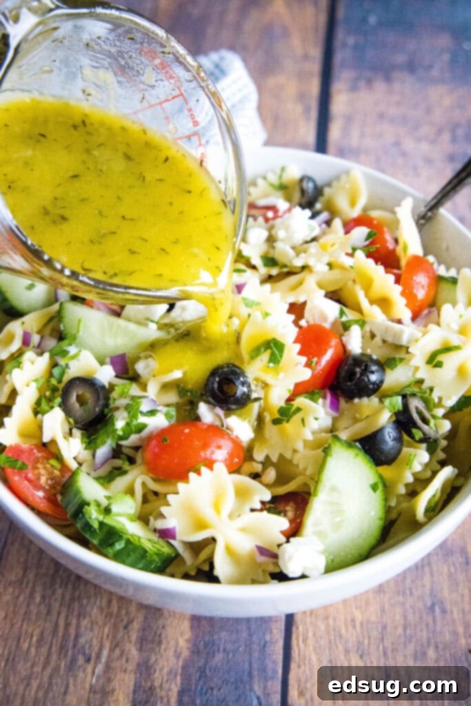 Zesty Greek Pasta Salad 4 pouring greek dressing over a bowl of pasta salad
