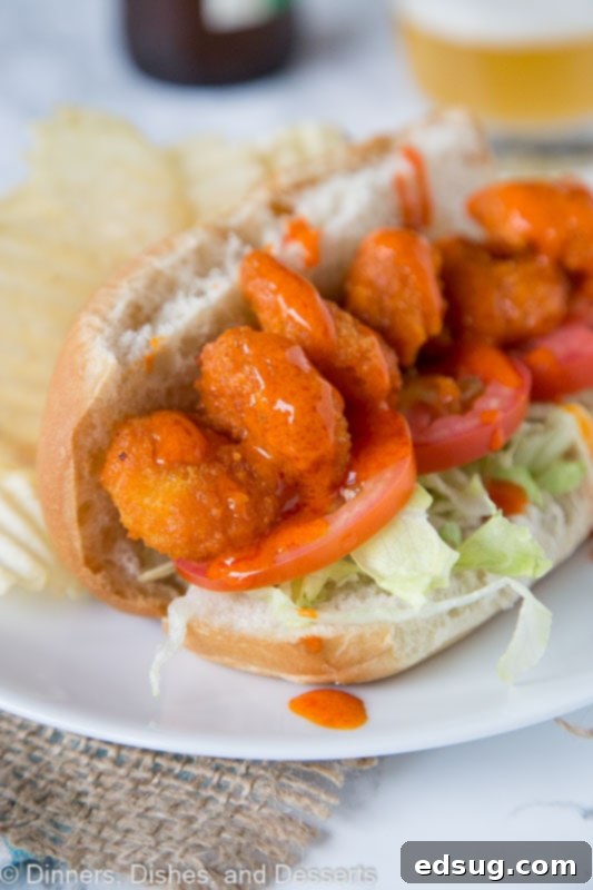 A vibrant plate featuring a perfectly assembled Buffalo Shrimp Po' Boy sandwich, garnished with fresh lettuce and tomato, served alongside a small dish of creamy ranch dressing, all on a rustic wooden table.