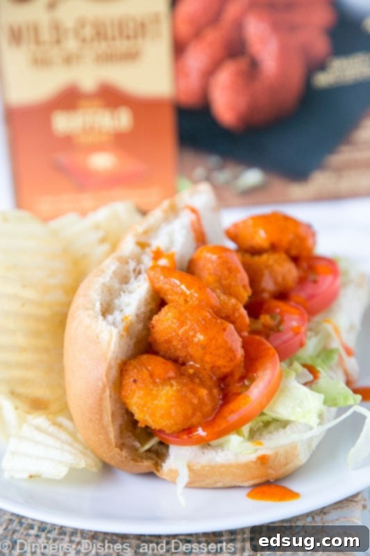 A close-up, appetizing view of a Buffalo Shrimp Po' Boy, showcasing the layers of crispy shrimp, fresh lettuce, and tomato, ready to be devoured, with a focus on the rich textures and vibrant colors.