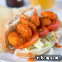 A close up of a delicious Buffalo Shrimp Po' Boy, featuring crispy shrimp spilling out of a toasted bun with fresh toppings.