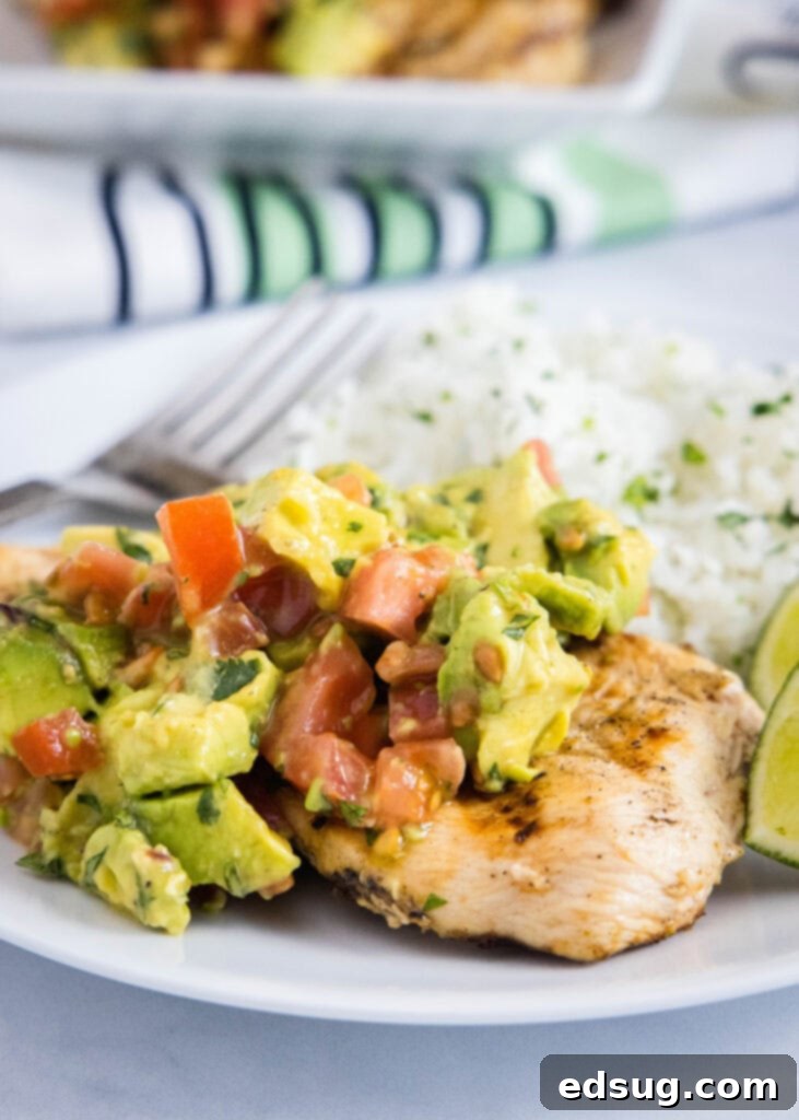 Close-up of grilled chicken topped generously with fresh avocado salsa and a lime wedge.