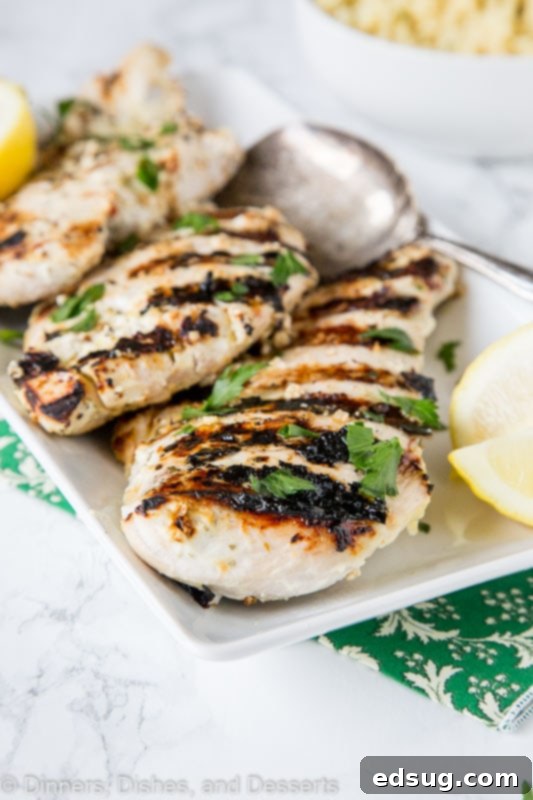 Perfectly Tender Yogurt Chicken 5 Close-up of a plate with succulent grilled chicken, garnished with fresh herbs and lemon wedges.