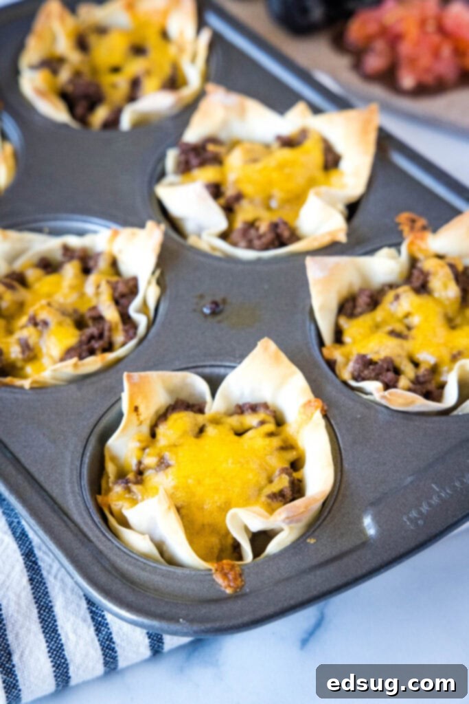 Several crispy taco cups, freshly baked and still warm in the muffin tin, showcasing their perfectly golden-brown wonton wrappers and bubbling melted cheese.