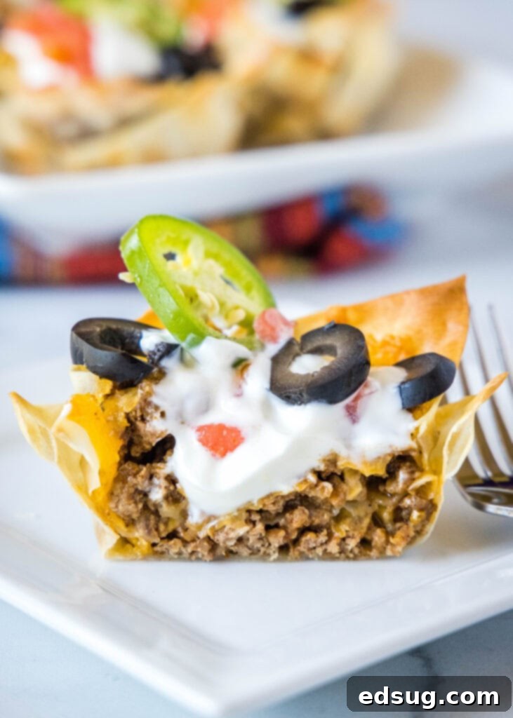 A perfectly crispy wonton taco cup, cut in half to showcase its delicious layers of seasoned ground meat and melted cheese, served elegantly on a clean white plate.