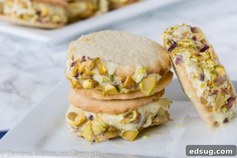 Three pistachio ice cream sandwich cookies on a white plate, showcasing the vibrant green chopped pistachios on the edges