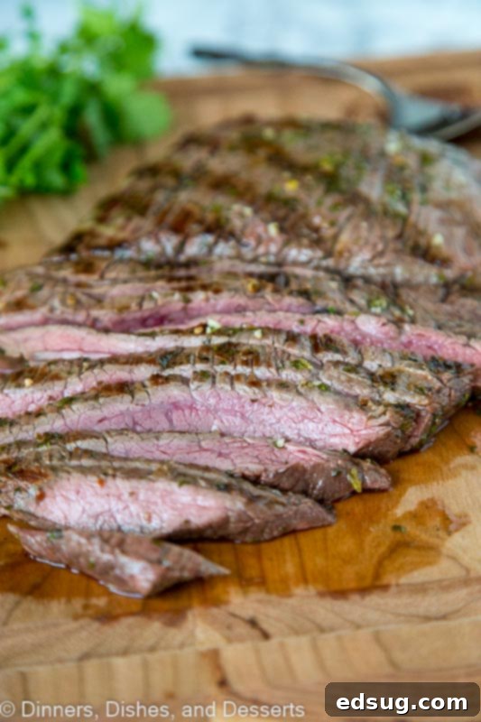 A close-up of a perfectly grilled and sliced chile lime flank steak, showing its tender interior and charred exterior, served on a cutting board with fresh cilantro and lime wedges.