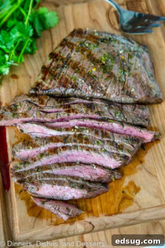 A perfectly sliced grilled flank steak resting on a wooden cutting board, ready to be served, highlighting its tender texture and the success of slicing against the grain. Often used for tacos.