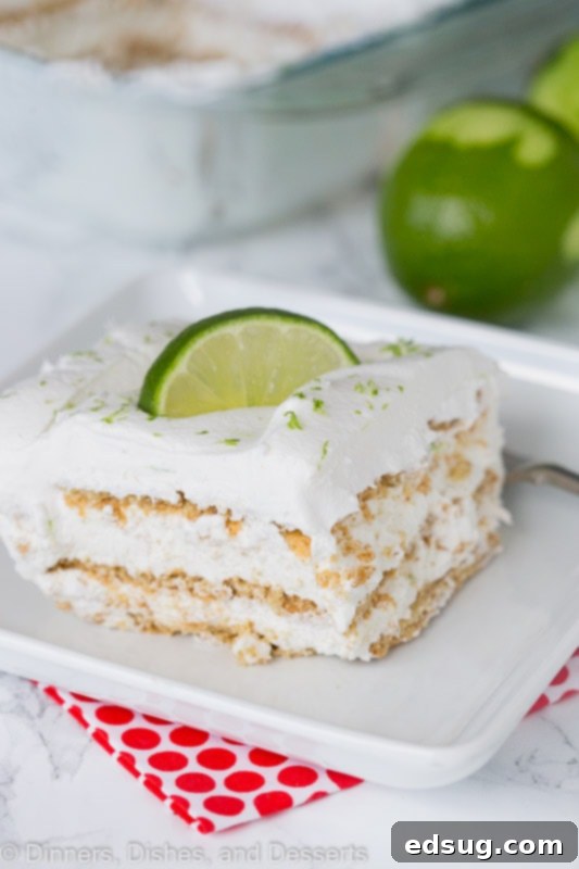 A perfectly portioned slice of key lime icebox cake on a white plate with a fork, showing the distinct layers