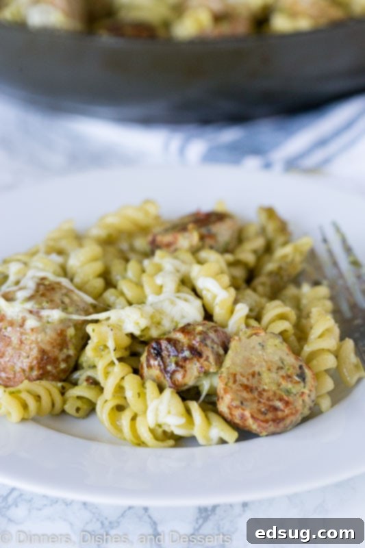 A vibrant plate of pesto pasta with meatballs, topped with fresh basil and parmesan cheese.