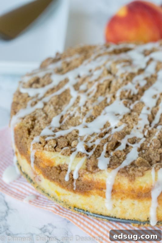 Dreamy Peaches and Cream Coffee Cake 2 A slice of moist peach coffee cake with a generous vanilla glaze drizzle on a white plate, showcasing the streusel topping and embedded peach pieces.