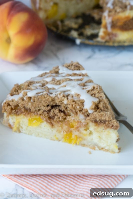 Dreamy Peaches and Cream Coffee Cake 3 A close-up shot of a single slice of peach coffee cake on a white plate, showing the streusel topping and succulent peaches within the moist cake.