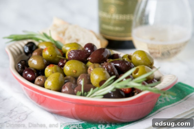 Close-up shot of a bowl brimming with roasted olives and a sprig of fresh rosemary on the side.