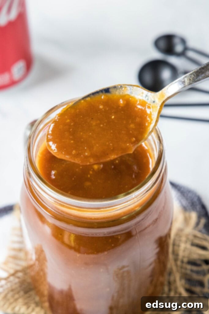 A close-up shot of a spoon dripping rich, thick BBQ sauce above a jar, ready for serving or storage.