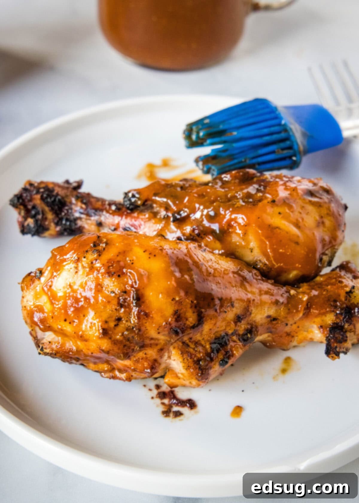 A succulent plate of barbecued chicken drumsticks glazed with homemade Coca-Cola BBQ sauce, with a basting brush nearby.