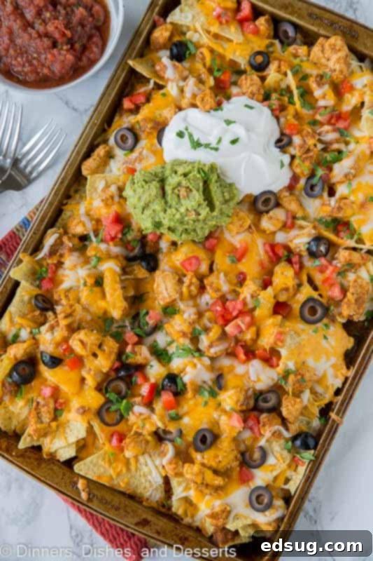 Loaded Sheet Pan Chicken Nachos 3 Freshly baked sheet pan chicken nachos with sides of creamy guacamole and sour cream.