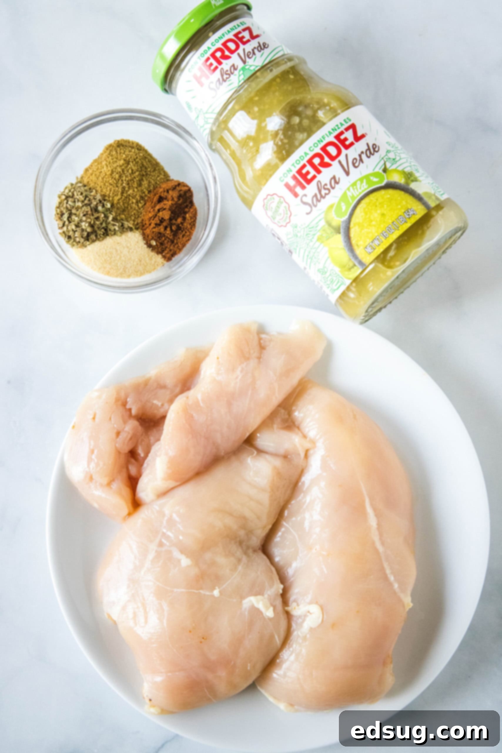 Learn how to cook juicy, flavorful salsa verde chicken in the Instant Pot with just two ingredients, a few spices, and 30 minutes! Essential ingredients for Instant Pot salsa verde chicken: chicken breasts, a jar of green salsa, and various spices arranged on a rustic wooden surface.
