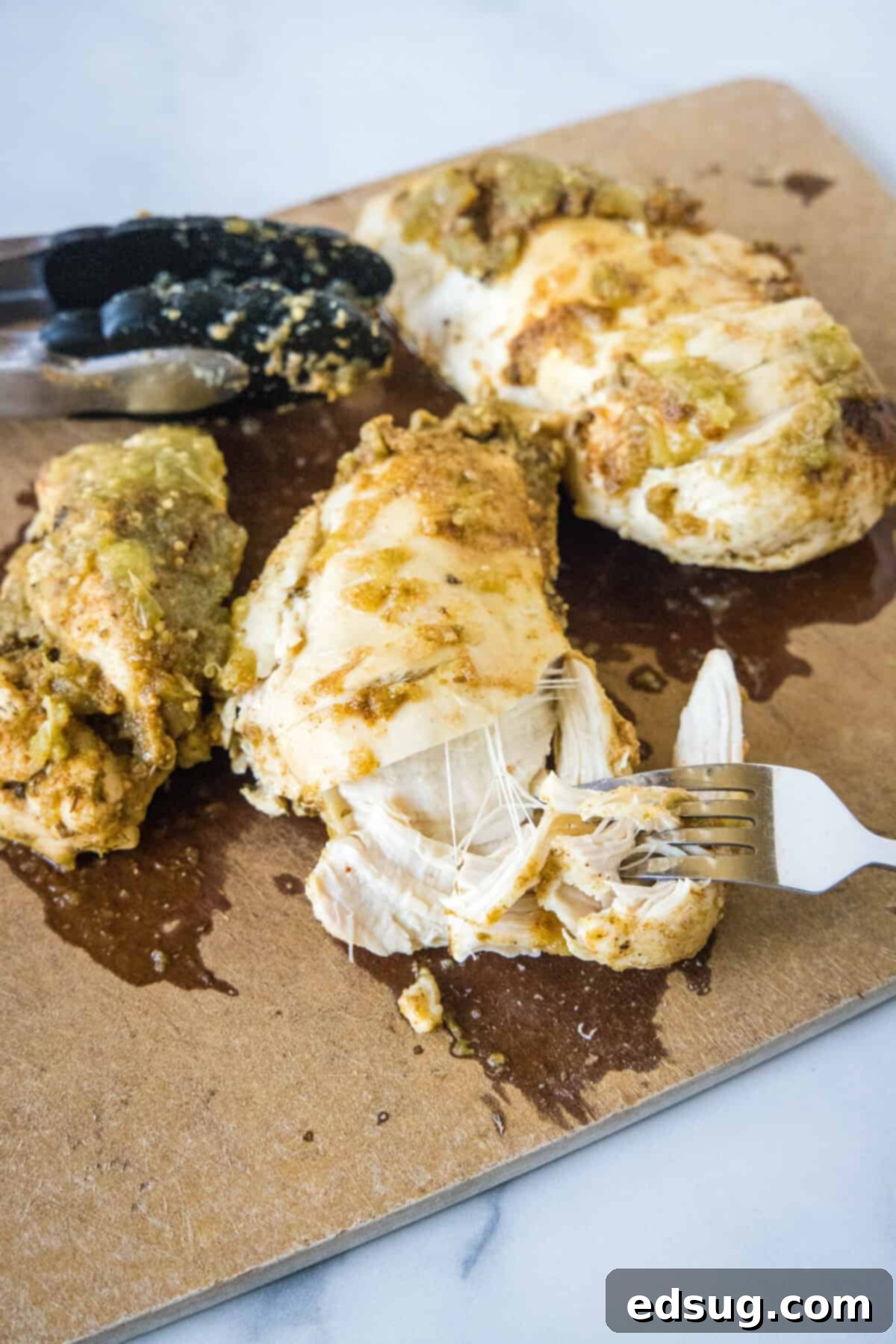 Learn how to cook juicy, flavorful salsa verde chicken in the Instant Pot with just two ingredients, a few spices, and 30 minutes! A fork effortlessly shredding a perfectly cooked salsa verde chicken breast on a cutting board, highlighting its tender texture.