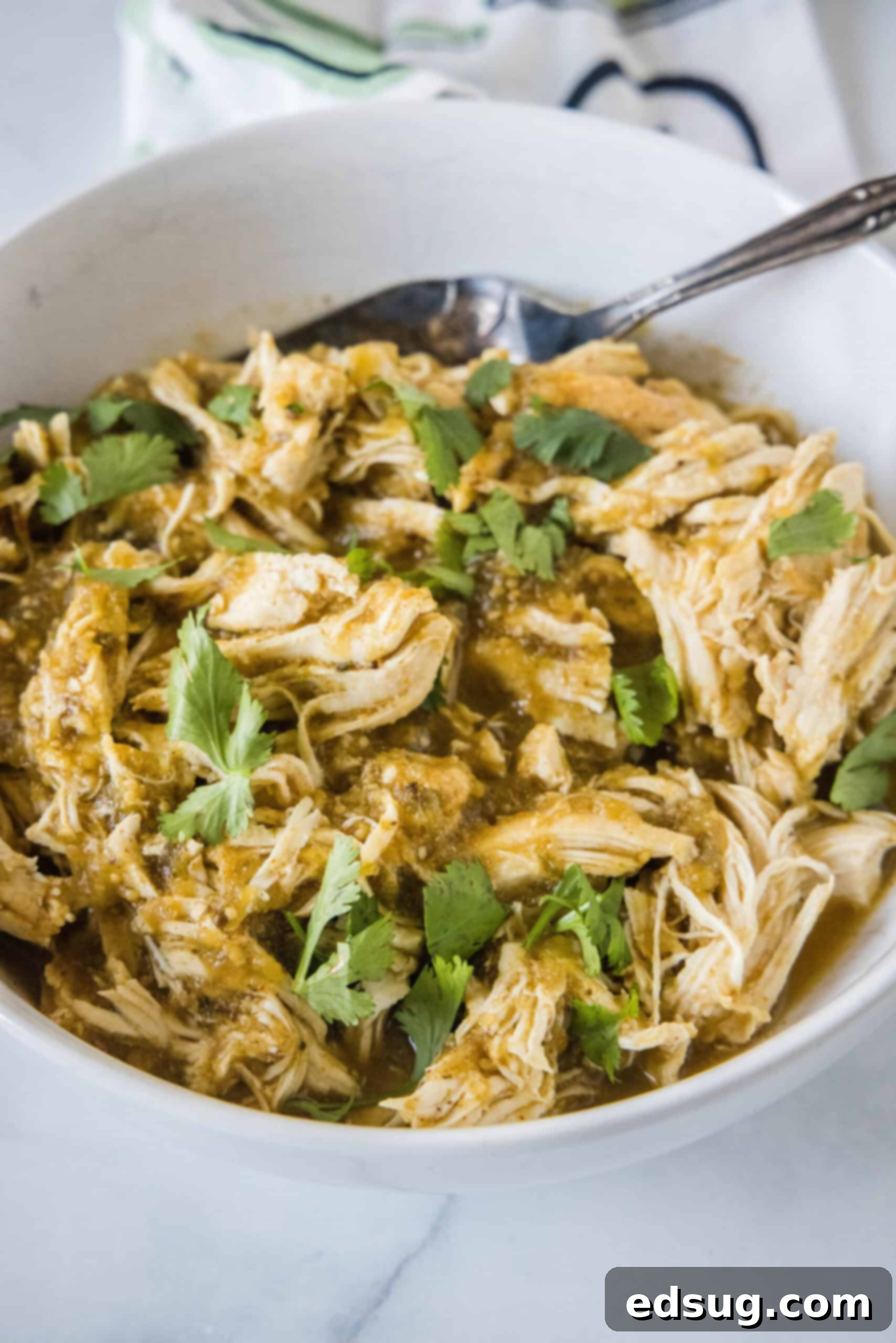 Learn how to cook juicy, flavorful salsa verde chicken in the Instant Pot with just two ingredients, a few spices, and 30 minutes! A generous serving of shredded salsa verde chicken in a white bowl, accompanied by a spoon, ready to be enjoyed.