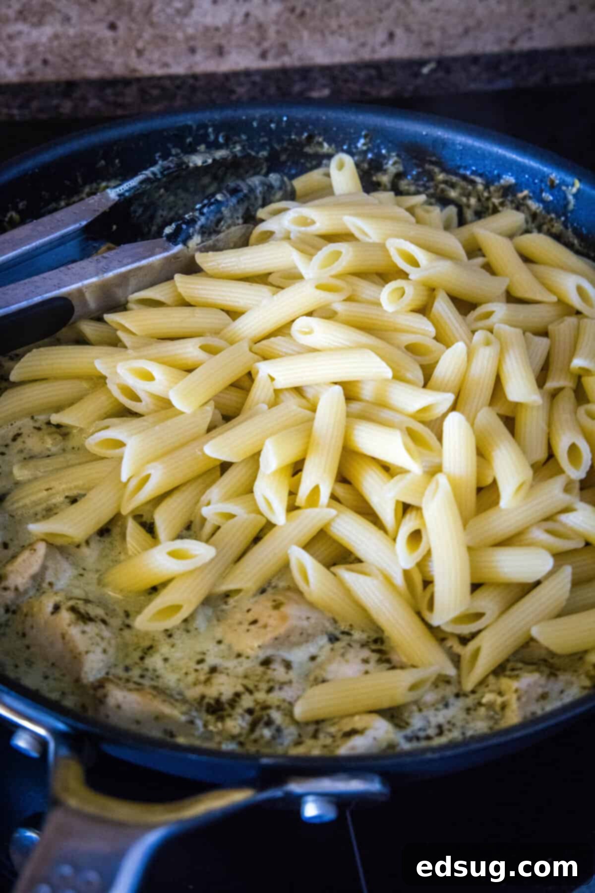 adding cooked pasta to skillet with pesto chicken sauce