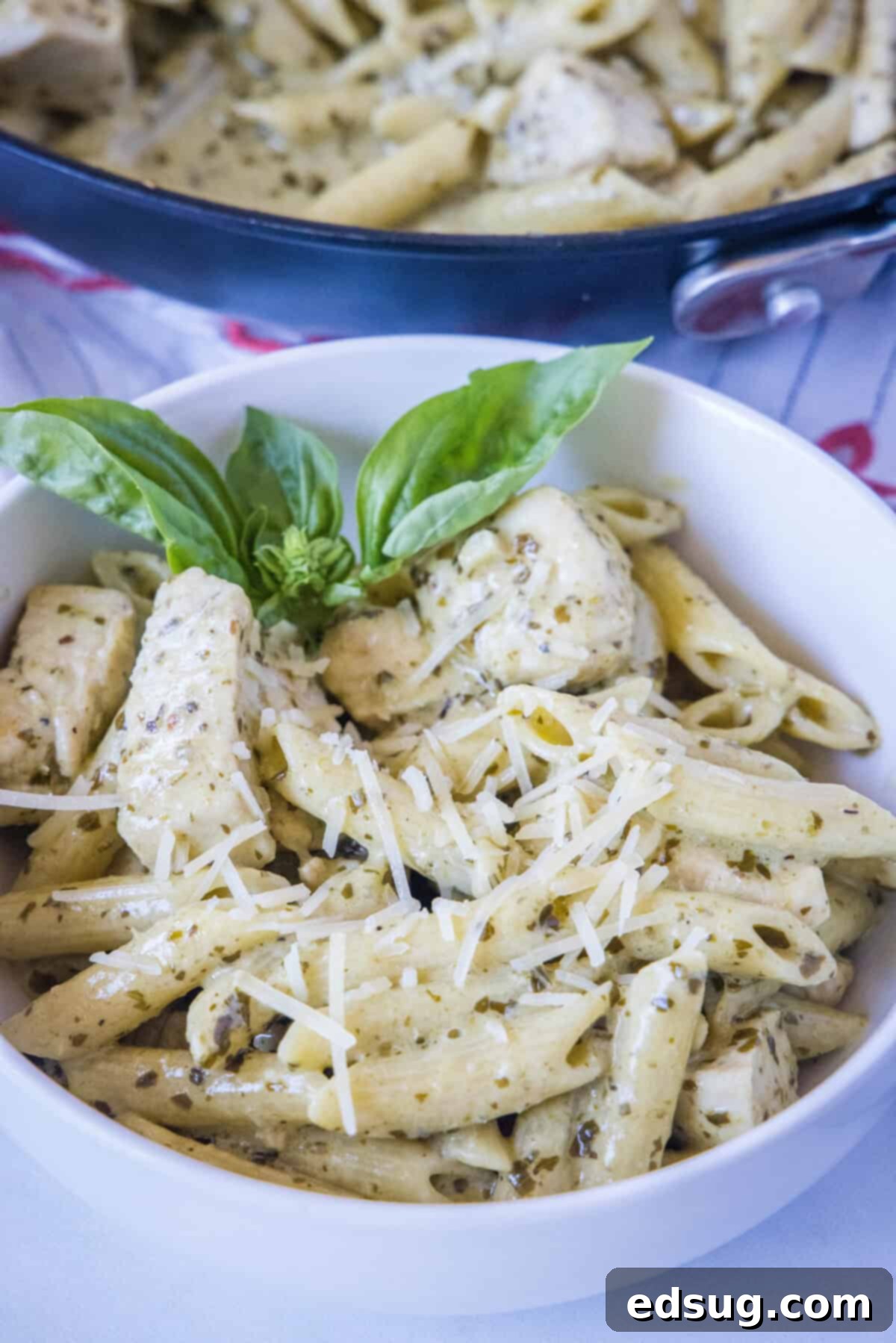 looking down on white bowl with chicken pesto pasta, garnished with fresh basil