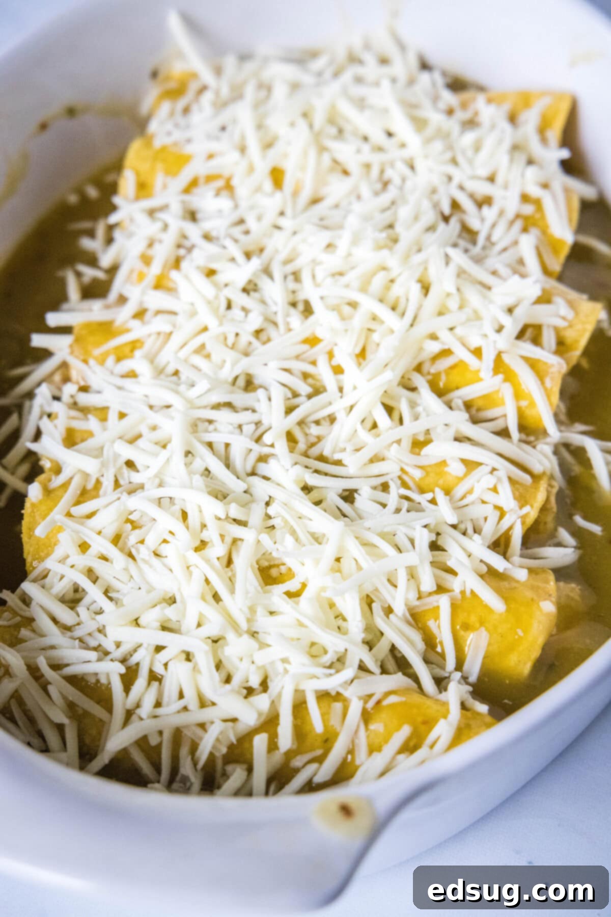 Zesty Green Chile Chicken Enchiladas 8 enchiladas topped with cheese ready to be baked