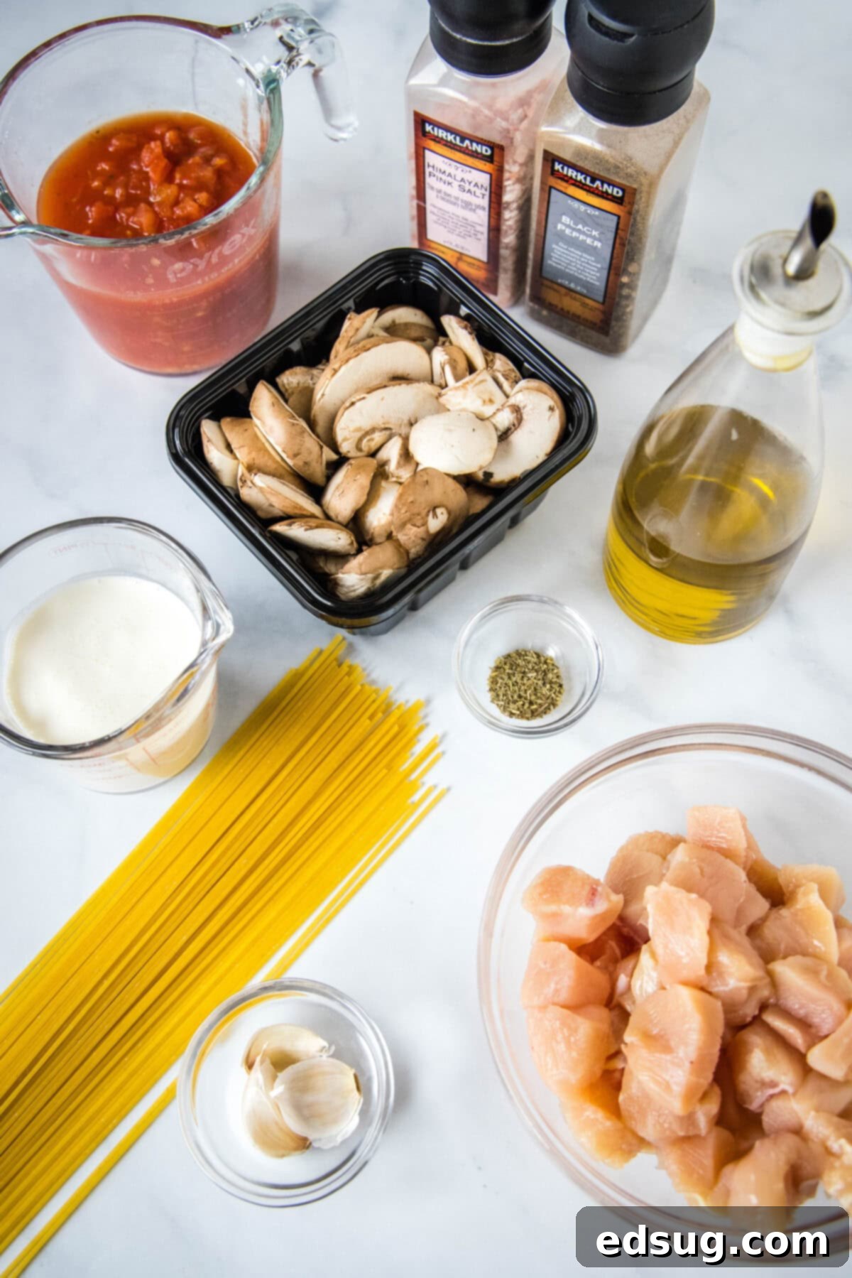 Creamy Tuscan Chicken Pasta 3 Fresh ingredients laid out on a wooden cutting board, including diced chicken breast, sliced mushrooms, garlic cloves, a can of diced tomatoes, and a carton of half-and-half, ready for making Tuscan chicken pasta.